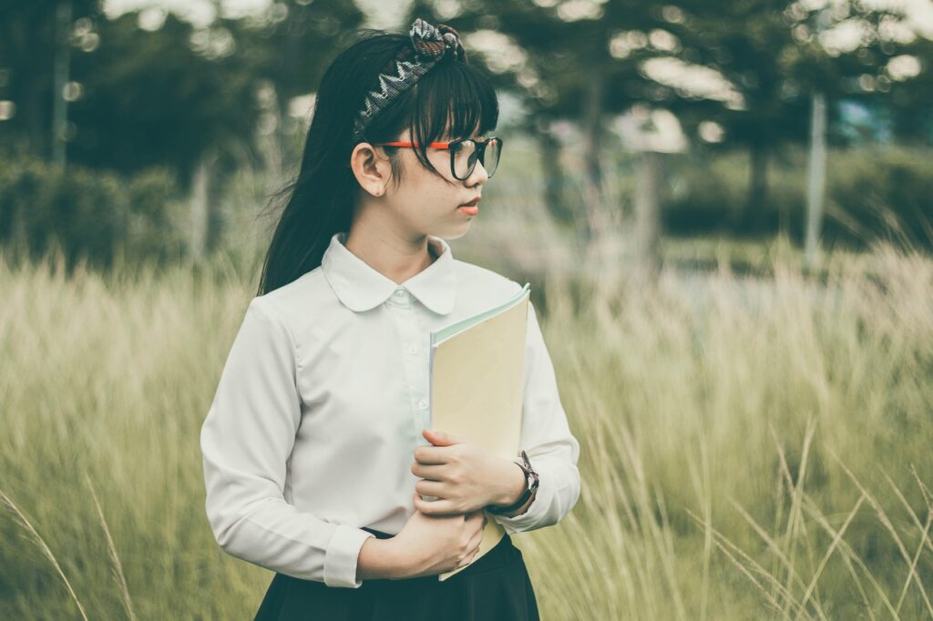 asian, student, book, child, girl, uniform, childcare near meschool uniform, eyeglasses, field, grass, kid, looking away, outdoors, nature, portrait. Child care near me daycare centre