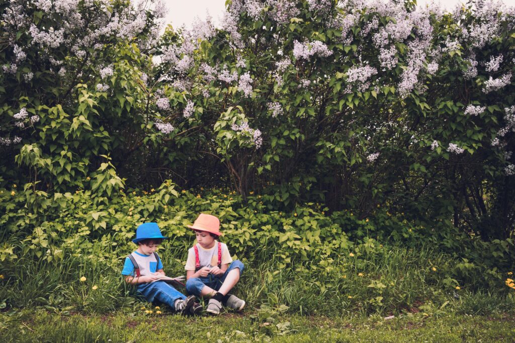 Two children sitting in a lush garden surrounded by blooming lilac bushes, enjoying a summer day. kid friendly gardening projects exploring nature