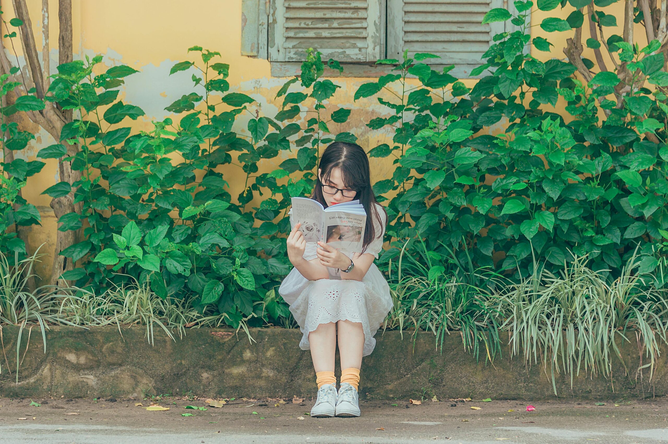 A young girl sits on a bench outdoors, immersed in a book with lush greenery around her. Earth Day activities for kids