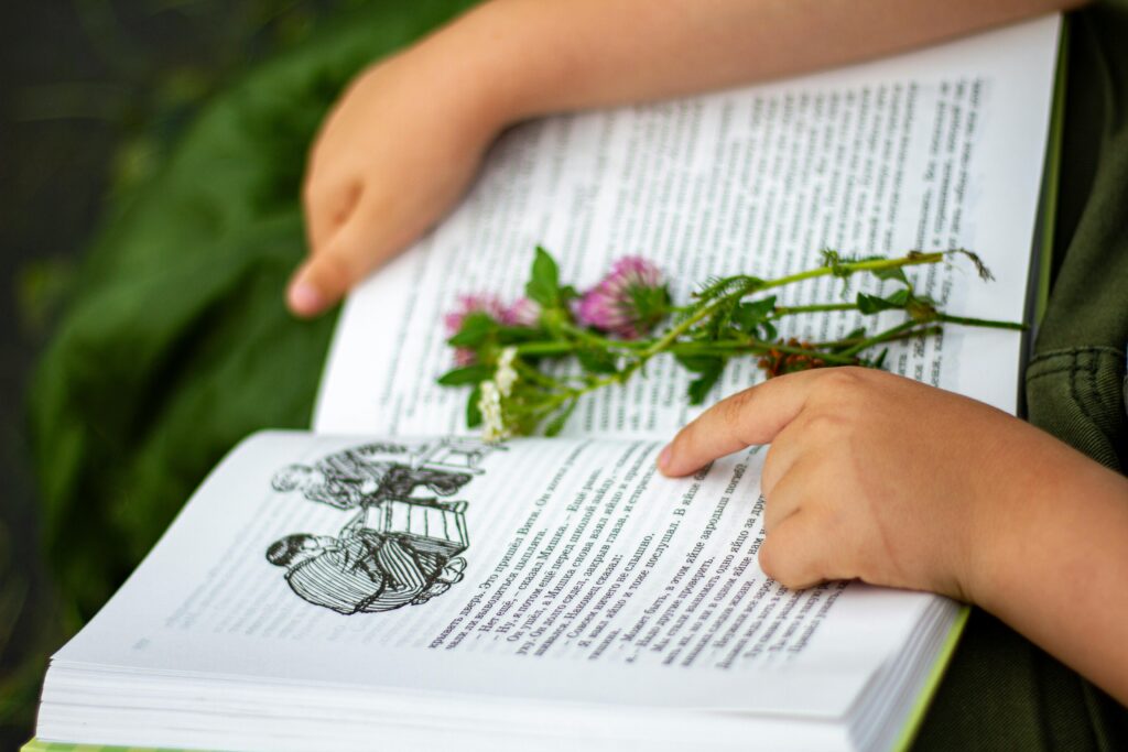 A child reading an open book with wildflowers placed on the pages, outdoors. environment education for kids nature craft with leaves and flowers